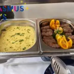 Püré és díszített húsrudak egymás melletti melegentartó tálakban